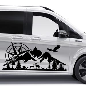 Könnte beinhalten: Ein schwarzer Vinyl-Aufkleber an der Seite eines weißen Lieferwagens. Das Design zeigt eine große Windrose, ein Gebirge, immergrüne Bäume sowie Silhouetten eines Hirsches, eines Fuchses und eines fliegenden Adlers am unteren Rand.