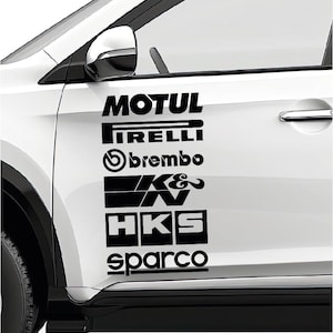 Puede incluir: En la puerta de un coche blanco, pegatinas negras muestran los logotipos de MOTUL, Pirelli, Brembo, K&N, HKS y Sparco. Los logotipos están apilados verticalmente, cada uno con una tipografía distinta.