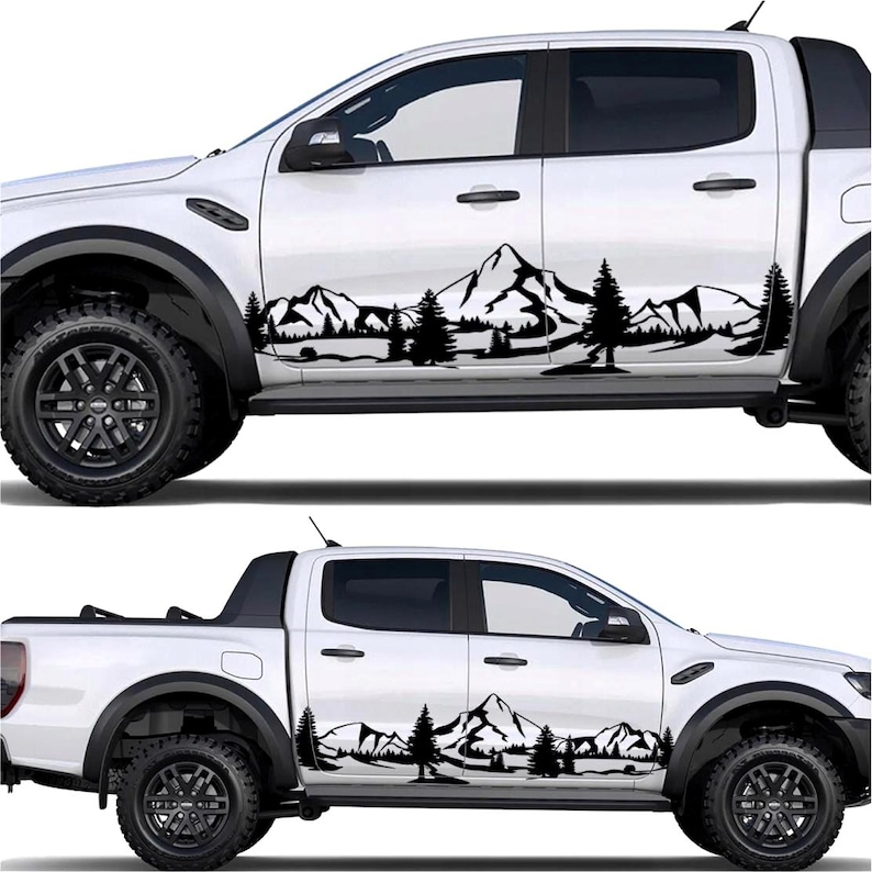 May include: White pickup truck with black mountain and tree decals on the side. The decals feature a silhouette of a mountain range and evergreen trees, creating a nature-themed design. The truck has black wheels and tires.