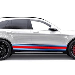 Puede incluir: SUV blanco con ruedas negras y pinzas de freno rojas. El vehículo presenta un diseño de franja de carreras en rojo, azul claro y azul oscuro a lo largo del lateral, añadiendo una estética deportiva.