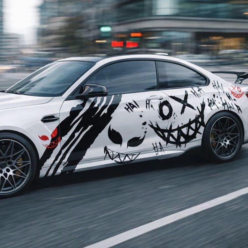 May include: A white two-door coupe car featuring black graphic decals on the side panel. The design includes stylized sharp-toothed faces, claw marks, and the repeated text "HA" in a black ink style, with a small red graphic accent near the front.