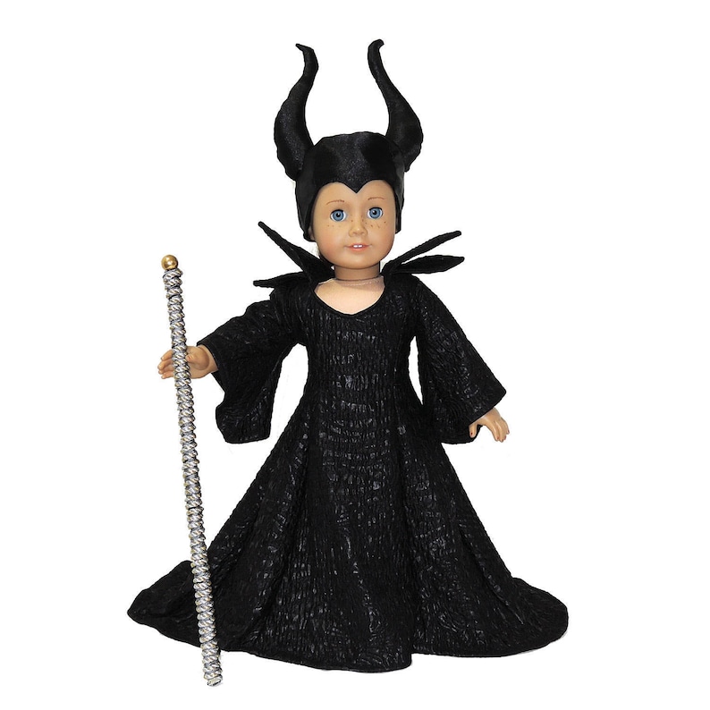 May include: A black doll dressed as Maleficent from the Disney movie "Sleeping Beauty". The doll is wearing a black dress with a long, flowing skirt and a black cape with a high collar. The doll has black horns and a black crown. The doll is holding a silver wand.