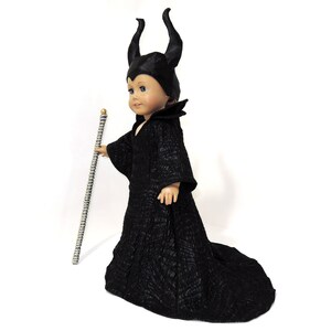 May include: A black doll dressed as Maleficent from the Disney movie Sleeping Beauty. The doll is wearing a black gown with a long train and a black horned headpiece. The doll is holding a gold and silver scepter.
