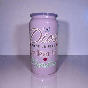 May include: A lavender-colored tumbler with a matching lid. The tumbler features the word "Dios" in a cursive font, a butterfly, and the phrase "TIENE UN PLAN que lleva tu Nombre" in white and green script, with red heart accents.