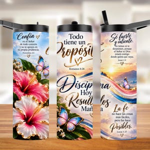 May include: A cylindrical tumbler with a black lid featuring a wrap-around design of pink and white hibiscus flowers, blue butterflies, and sunset clouds. The tumbler displays Spanish religious text including verses like Proverbios 3:5 and Romanos 8:28.