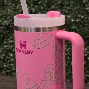 Puede incluir: Taza Stanley rosa con borde y asa blancos. La taza presenta un dise&ntilde;o floral y una pajita transparente. El logotipo de Stanley es visible en el lateral. La taza est&aacute; dise&ntilde;ada para bebidas fr&iacute;as o calientes.