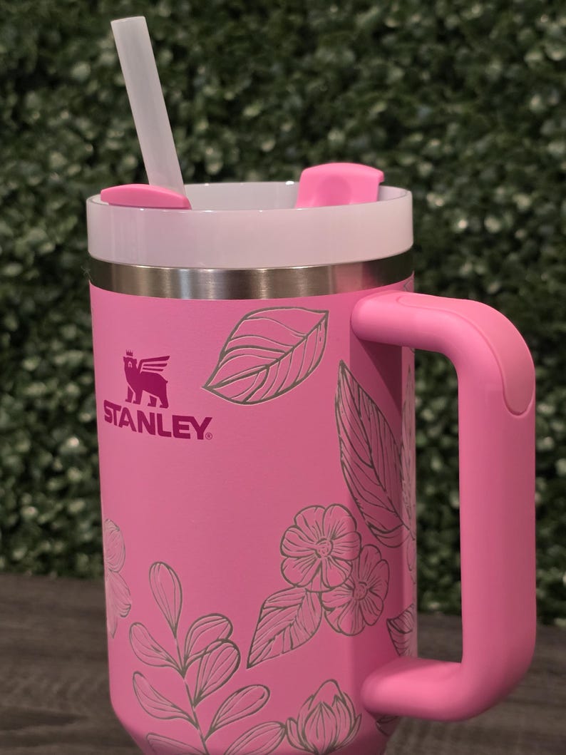 Puede incluir: Taza Stanley rosa con borde y asa blancos. La taza presenta un dise&ntilde;o floral y una pajita transparente. El logotipo de Stanley es visible en el lateral. La taza est&aacute; dise&ntilde;ada para bebidas fr&iacute;as o calientes.