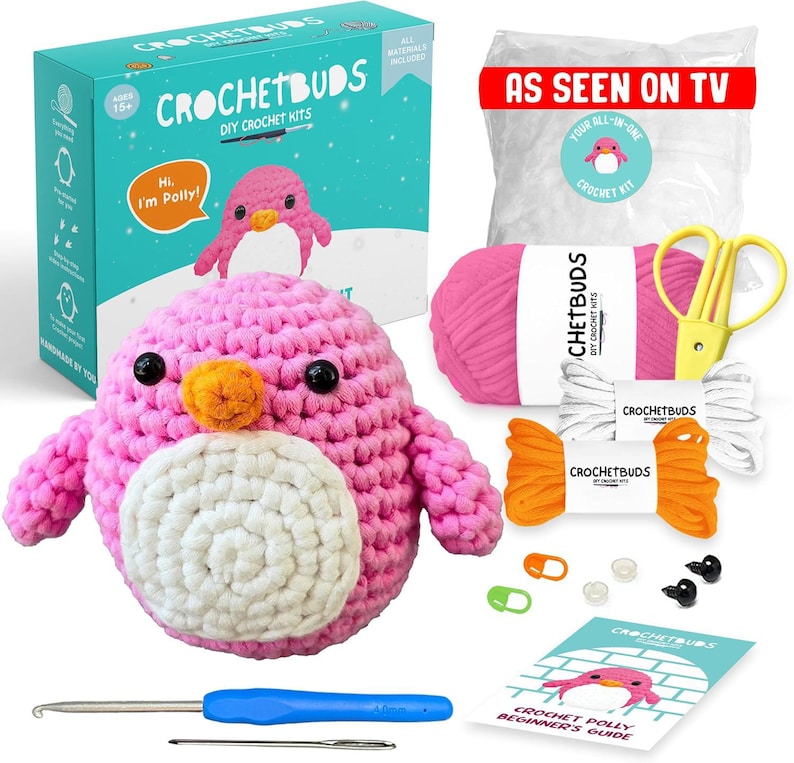 May include: A pink crocheted penguin DIY kit with a blue handle crochet hook, scissors, yarn, and a beginner's guide. The kit includes a box with the text "CROCHETBUDS DIY CROCHET KITS" and "Hi, I'm Polly!"