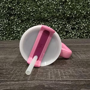 Puede incluir: Una tapa de vaso para sorber rosa y blanca con un asa rosa a juego y una pajita blanca. La tapa tiene un acento rosa oscuro y un peque&ntilde;o logotipo. La taza est&aacute; dise&ntilde;ada para beber f&aacute;cilmente.