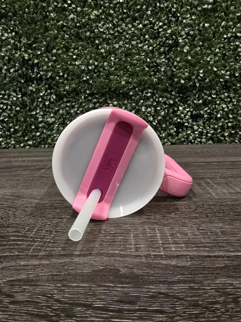 Puede incluir: Una tapa de vaso para sorber rosa y blanca con un asa rosa a juego y una pajita blanca. La tapa tiene un acento rosa oscuro y un peque&ntilde;o logotipo. La taza est&aacute; dise&ntilde;ada para beber f&aacute;cilmente.