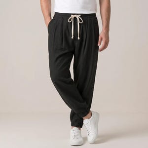 Könnte beinhalten: Schwarze Hose mit lockerer Passform, elastischem Bund mit beigem Kordelzug und Bündchen an den Knöcheln. Die Hose wird mit einem schlichten weißen T-Shirt und sauberen weißen Turnschuhen kombiniert und zeigt ein einfaches, funktionales Design.