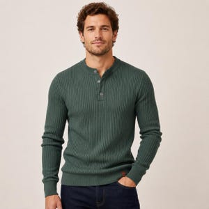 Puede incluir: Una camiseta henley de manga larga en color verde oscuro con textura acanalada vertical, tapeta con tres botones pequeños y una pequeña etiqueta rectangular marrón cerca del dobladillo inferior, combinada con vaqueros azul oscuro.