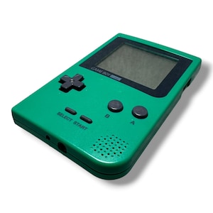 May include: A green handheld video game console with a black screen border, a directional pad, A and B buttons, and Select and Start buttons. The device features the text GAME BOY pocket printed below the screen and a speaker grille on the front.