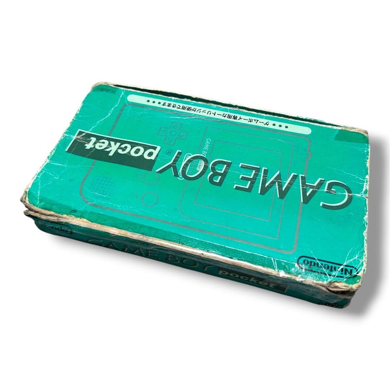 May include: A rectangular teal cardboard box for a Game Boy Pocket handheld gaming console. The box features the text GAME BOY pocket in large white letters, with additional Japanese text and a line drawing of the console on the front surface.