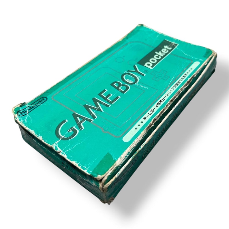 May include: A teal-colored rectangular cardboard box for a Nintendo Game Boy Pocket handheld gaming console. The box features the text GAME BOY pocket and Nintendo logo, showing significant wear, creasing, and edge damage on the exterior.