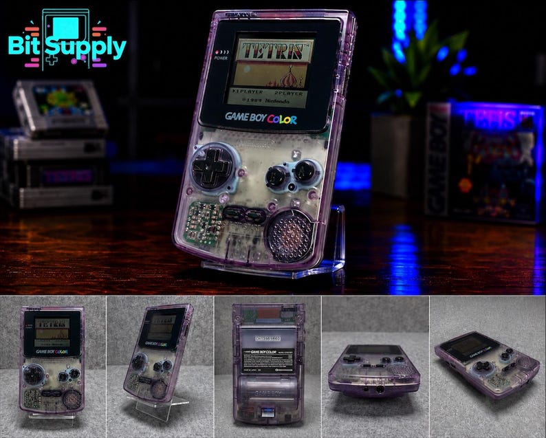 May include: A transparent purple Game Boy Color handheld gaming console featuring a black screen bezel, a directional pad, two action buttons, and a speaker. The device displays the Tetris game title on its screen and includes a battery compartment.