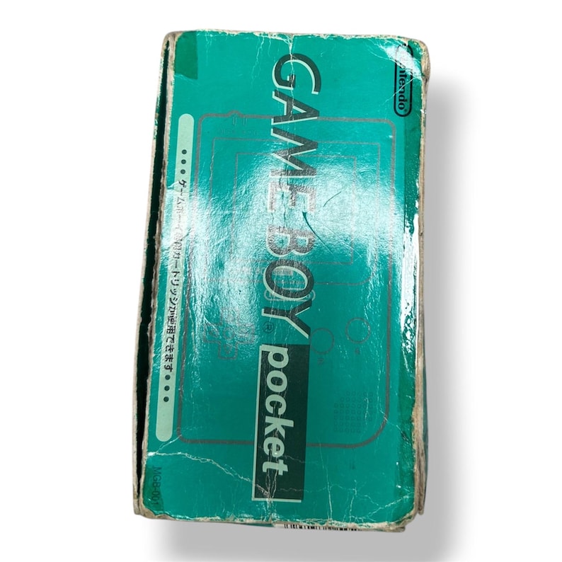 May include: A rectangular teal cardboard box for a Nintendo Game Boy Pocket handheld gaming console. The front features the text GAME BOY pocket in white and black, a Nintendo logo, and Japanese text along the left side. The box shows visible wear.