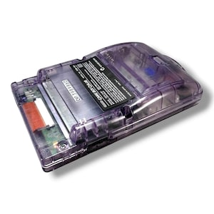 May include: A translucent purple handheld game console with a visible internal battery compartment and circuit board. The back features a black label with white text reading GAME BOY COLOR, model number CGB-001, and serial number CH13989860.