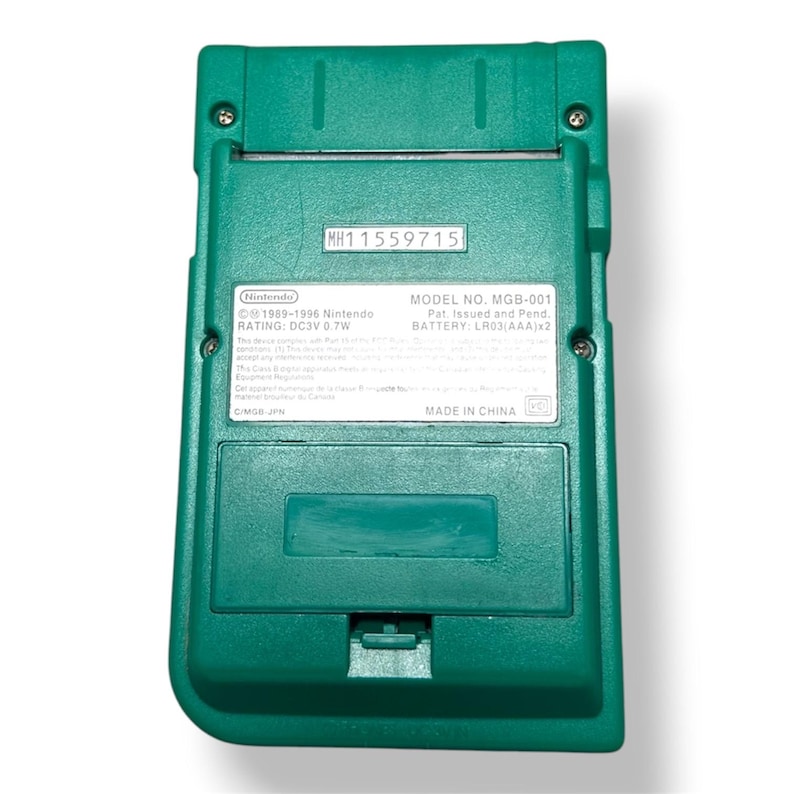 May include: A teal handheld gaming console, specifically the Nintendo Game Boy Pocket model MGB-001. The back view shows a battery compartment cover, a serial number label MH11559715, and technical specifications including DC3V 0.7W power rating.