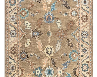 May include: Rectangular area rug with a central brown field and an intricate pattern of floral and geometric designs in shades of blue, beige, and brown. The rug has a cream-colored border with repeating floral motifs, creating a traditional aesthetic.