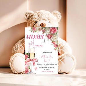 Puede incluir: Una tarjeta de invitación para un brunch del Día de la Madre con las palabras "MOMS and Mimosas" en escritura rosa. La tarjeta incluye una copa de champán con un lazo rosa, rodeada de flores rosas y blancas. La invitación la sostiene un oso de peluche.