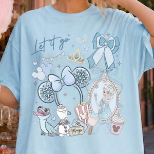May include: A light blue t-shirt featuring a graphic print with the text Let it go, a character in a mirror, a snowman, a lizard, mouse ears, a bow, and a popcorn bucket. The design includes various snowflake and star accents in shades of blue and white.