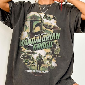 Pu&ograve; includere: T-shirt grigio scuro con grafica di Star Wars: The Mandalorian. Il design include il Mandaloriano, Grogu e il testo "THE MANDALORIAN AND GROGU" e "THIS IS THE WAY". La maglietta &egrave; etichettata "COMFORT COLORS Pepper".