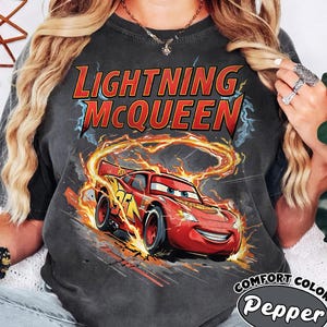 Puede incluir: Camiseta gris oscuro con Lightning McQueen de la pel&iacute;cula Cars. El gr&aacute;fico muestra el coche de carreras rojo con llamas y el texto "Lightning McQueen". La camiseta est&aacute; etiquetada como "Comfort Colors Pepper".