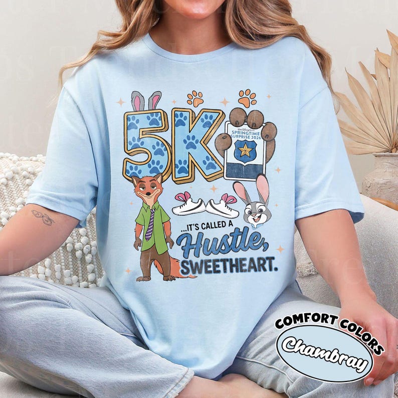 Puede incluir: Camiseta azul claro con un dise&ntilde;o de zorro y conejo, huellas de patas y el texto "5K". La camiseta tambi&eacute;n tiene el texto "...IT'S CALLED A Hustle, SWEETHEART."
