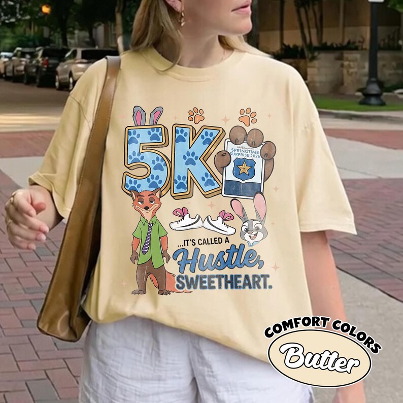 Puede incluir: Camiseta Comfort Colors color mantequilla con un dise&ntilde;o 5K, huellas de patas y personajes de dibujos animados. La camiseta incluye el texto "...IT'S CALLED A HUSTLE, SWEETHEART." y "SPRINGTIME SURPRISE 2024".