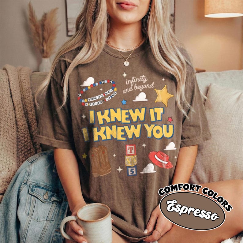 Pode incluir: Uma t-shirt cor de caf&eacute; expresso com uma estampa gr&aacute;fica com o texto I KNEW IT I KNEW YOU, infinity and beyond, e You've got a friend in me. O design inclui uma pulseira de contas, uma estrela amarela, uma bota de cowboy, blocos e um chap&eacute;u vermelho.