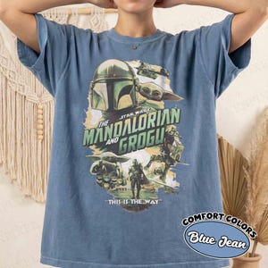 Pu&ograve; includere: T-shirt blu jeans con grafica di Star Wars con "The Mandalorian and Grogu". Il design include personaggi e la frase "THIS IS THE WAY". La maglietta &egrave; etichettata "COMFORT COLORS".
