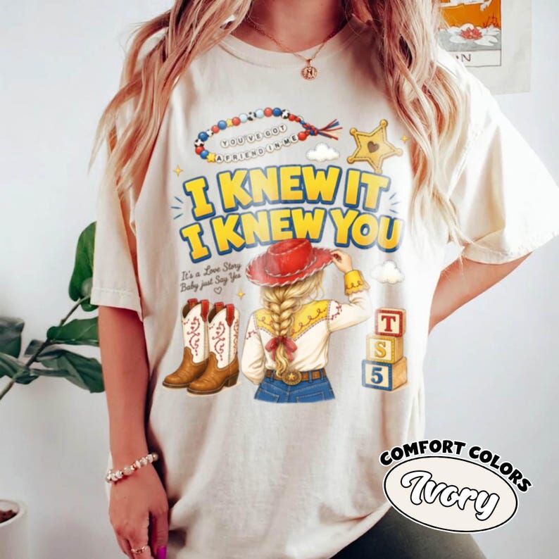 May include: An ivory t-shirt featuring a graphic print with the text I KNEW IT I KNEW YOU, a beaded necklace, a yellow star, a pair of brown cowboy boots, a blonde character wearing a red hat, and three stacked blocks labelled T, S, and 5.