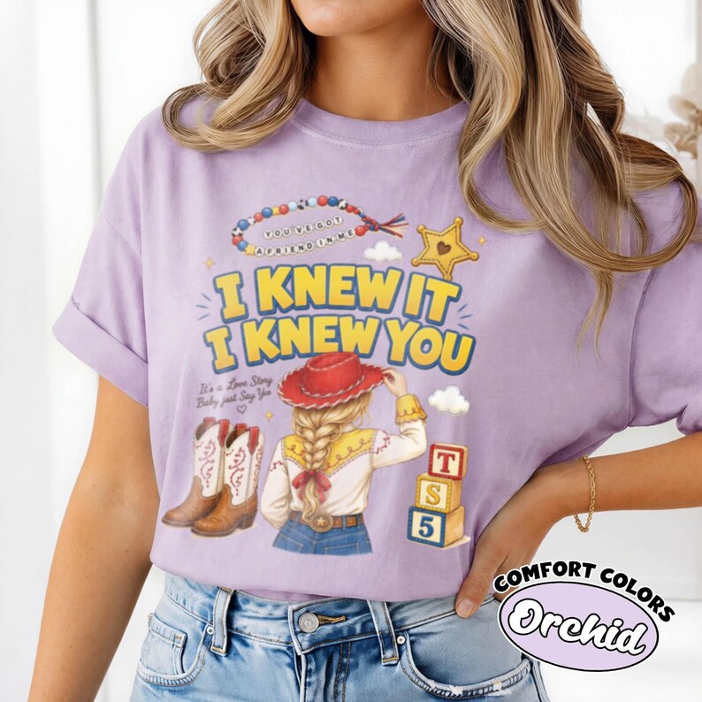 May include: A light purple t-shirt featuring a graphic print with the text I KNEW IT I KNEW YOU, a beaded necklace, a yellow star, a cowgirl with a red hat and blonde braid, cowboy boots, and three stacked alphabet blocks labelled T, S, and 5.