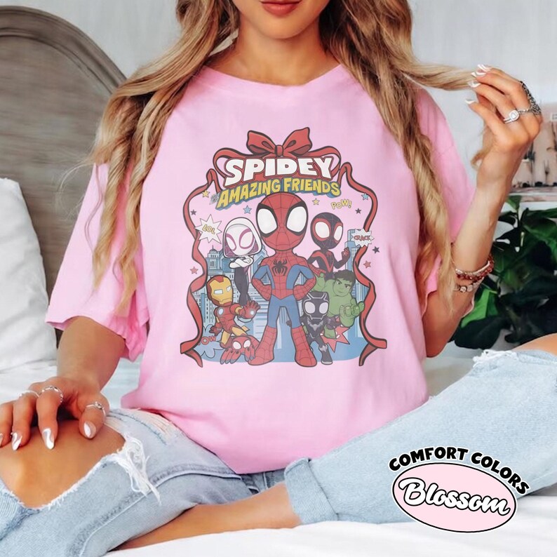 May include: Pink t-shirt featuring the text "Spidey Amazing Friends" with cartoon illustrations of Spider-Man and other characters. The shirt is a Comfort Colors Blossom tee.