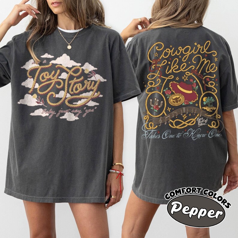 May include: A charcoal gray t-shirt featuring a front graphic of clouds and the text Toy Story with the phrase baby, just say yes. The back graphic displays a rope design, a hat, and the text Cowgirl Like Me, Takes One to Know One.