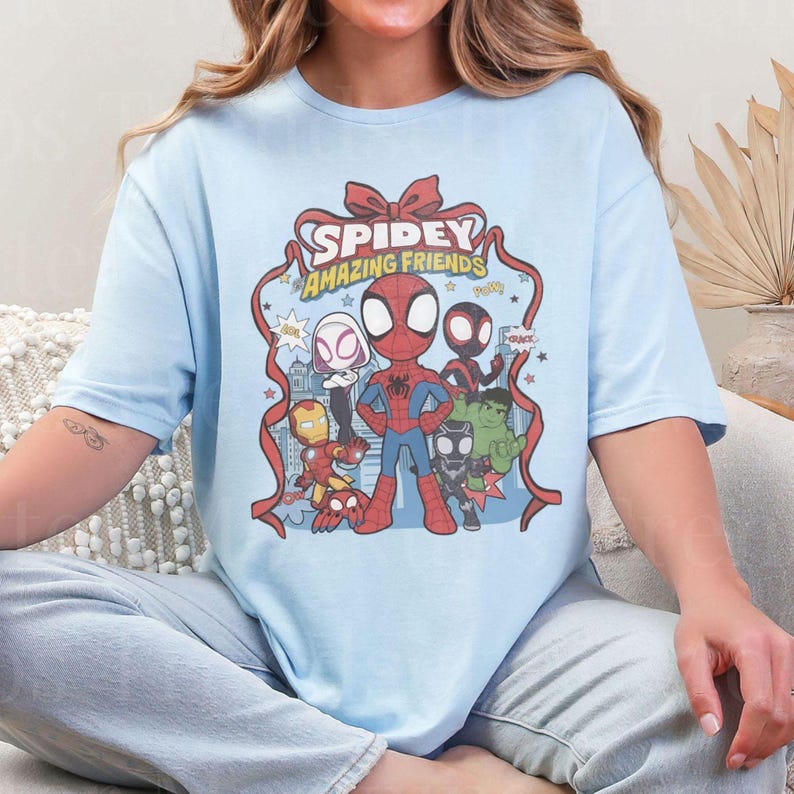 May include: Light blue t-shirt featuring a graphic of Spidey and his Amazing Friends. The design includes Spider-Man, Iron Man, Hulk, and other characters. The text "Spidey Amazing Friends" is displayed above the characters.