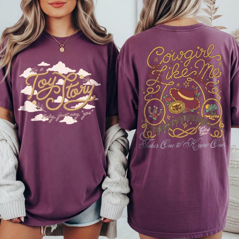 May include: A plum-colored t-shirt featuring a front graphic with the text Toy Story in rope-style lettering against white clouds. The back graphic displays the text Cowgirl Like Me with rope borders, a cowboy hat, and musical notes.