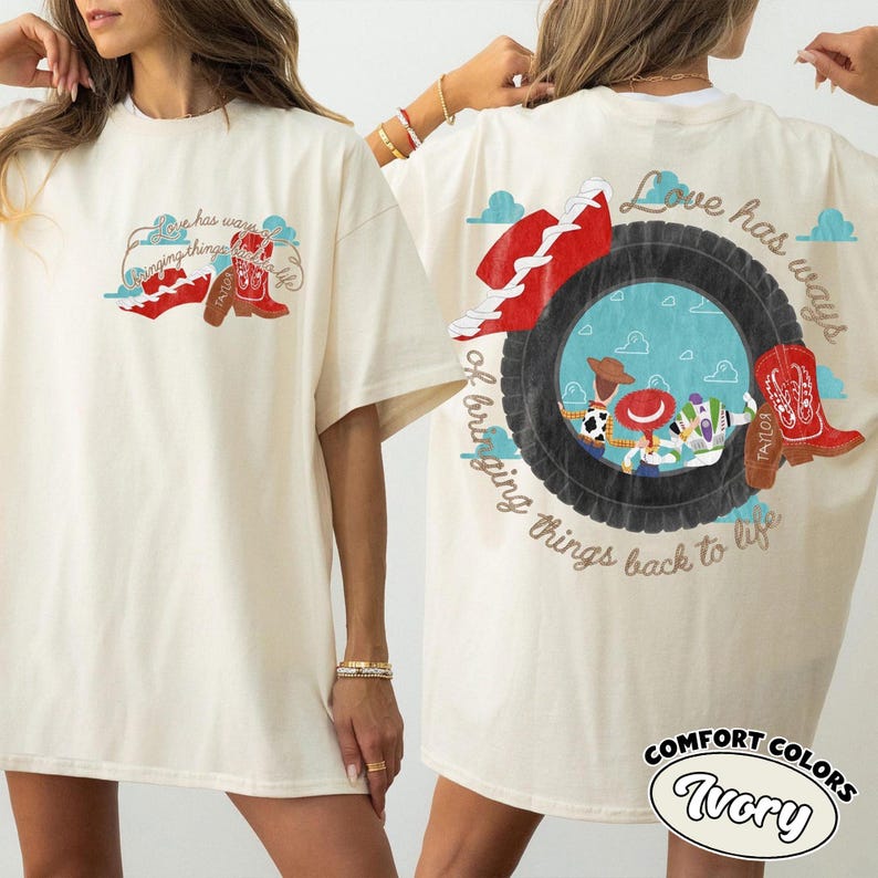 May include: An ivory short-sleeve t-shirt featuring a graphic print of a tire, a red cowboy boot, and characters from Toy Story. The text "Love has ways of bringing things back to life" is printed in a cursive font around the tire graphic.