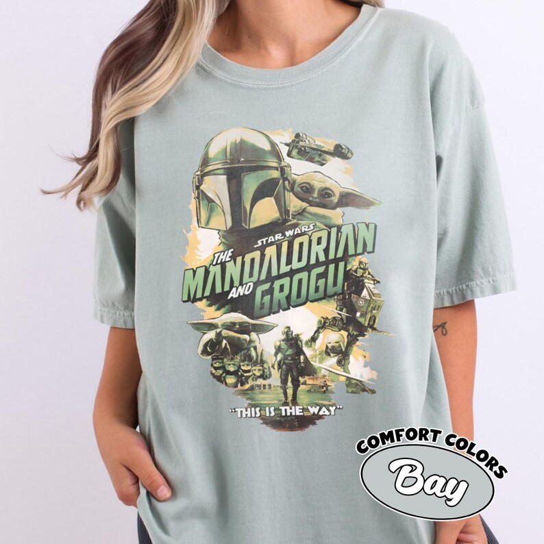 Pu&ograve; includere: T-shirt verde salvia con grafica della serie Star Wars, "The Mandalorian and Grogu". Il design include il casco Mandaloriano, Grogu e la frase "This is the Way".