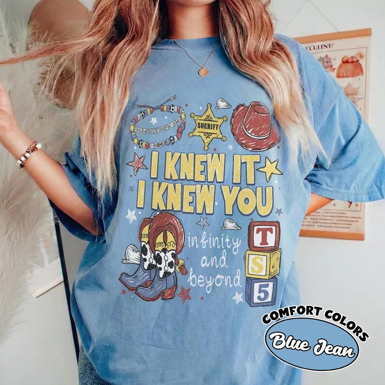 May include: A blue t-shirt featuring a graphic print with the text I KNEW IT I KNEW YOU and infinity and beyond. The design includes a sheriff badge, a cowboy hat, a beaded bracelet, cowboy boots, and three stacked blocks labeled T, S, and 5.