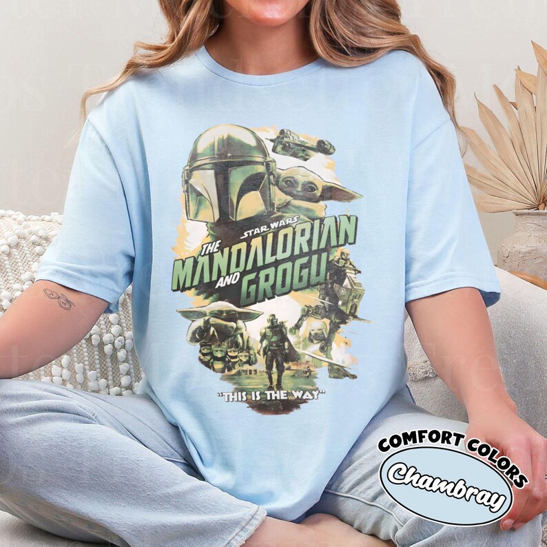 Pu&ograve; includere: T-shirt azzurra con grafica della serie Star Wars, "The Mandalorian and Grogu." Il design include immagini del Mandaloriano, Grogu e un'astronave, con la frase "This is the Way."