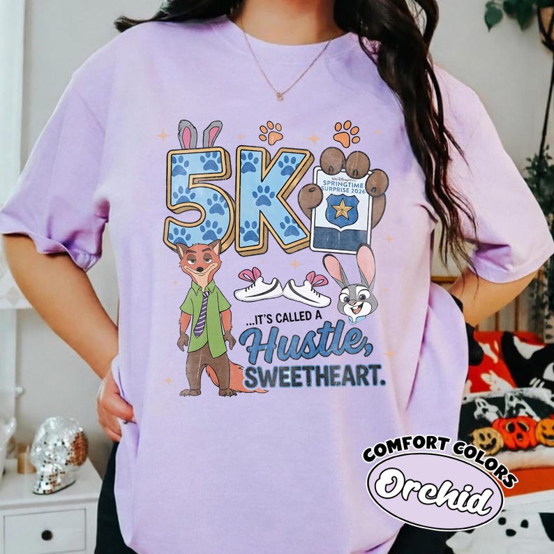 Puede incluir: Una camiseta de color lila claro con un dise&ntilde;o gr&aacute;fico de dibujos animados y el texto "5K". El dise&ntilde;o incluye las palabras "...IT'S CALLED A Hustle, Sweetheart." y "Springtime Surprise 2024". La camiseta tambi&eacute;n tiene las palabras "Comfort Colors" y "Orchid".