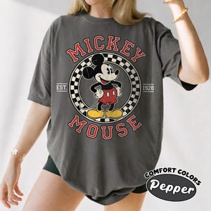 May include: Dark gray t-shirt featuring a vintage Mickey Mouse graphic. The design includes Mickey in a circle with the words "Mickey Mouse" and "Est. 1928." The shirt is labeled "Comfort Colors Pepper."