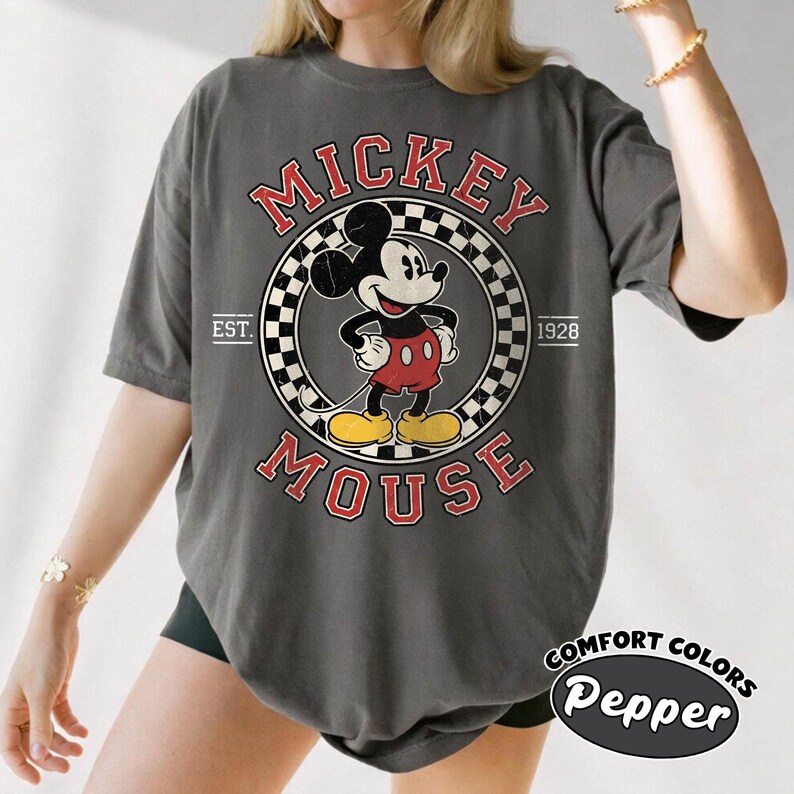 May include: Dark gray t-shirt featuring a vintage Mickey Mouse graphic. The design includes Mickey in a circle with the words "Mickey Mouse" and "Est. 1928." The shirt is labeled "Comfort Colors Pepper."