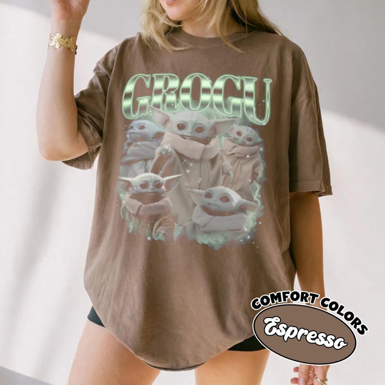 May include: A brown short-sleeve t-shirt featuring a graphic print of multiple Grogu characters. The text GROGU appears in a large, stylized, light green font above the characters. The design includes subtle light green glowing accents.