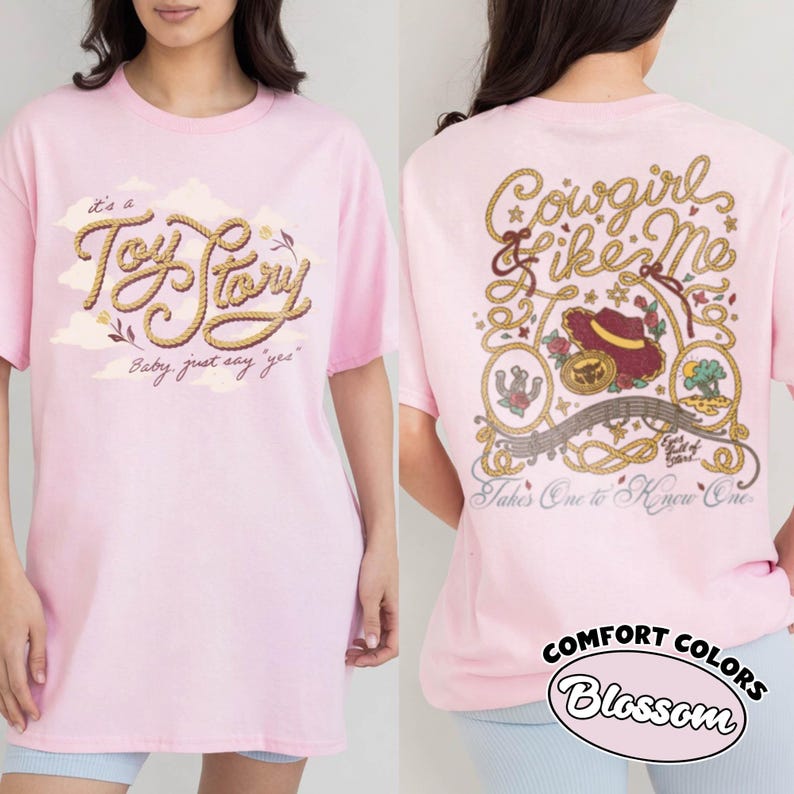May include: A light pink t-shirt featuring a front graphic with the text "it's a Toy Story Baby, just say 'yes'" in rope-style lettering. The back graphic displays "Cowgirl like Me" and "Takes One to Know One" with illustrations of a hat and rope.