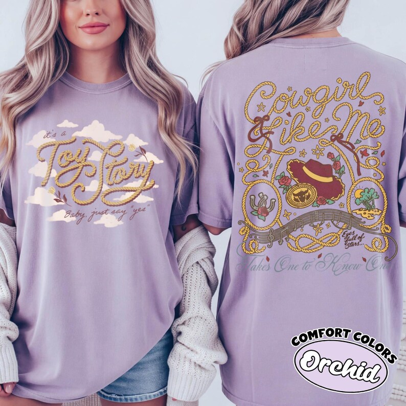 May include: A light purple t-shirt featuring a front graphic with the text Toy Story and clouds, and a back graphic with the text Cowgirl Like Me, a cowboy hat, a horseshoe, and a landscape illustration, all rendered in a rope-style font design.
