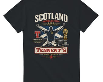 May include: Black t-shirt with a graphic celebrating Scotland's World Cup 2026. The design includes the word "Scotland", a soccer player, a trophy, and "Tennent's" branding. The shirt is proudly Scottish.