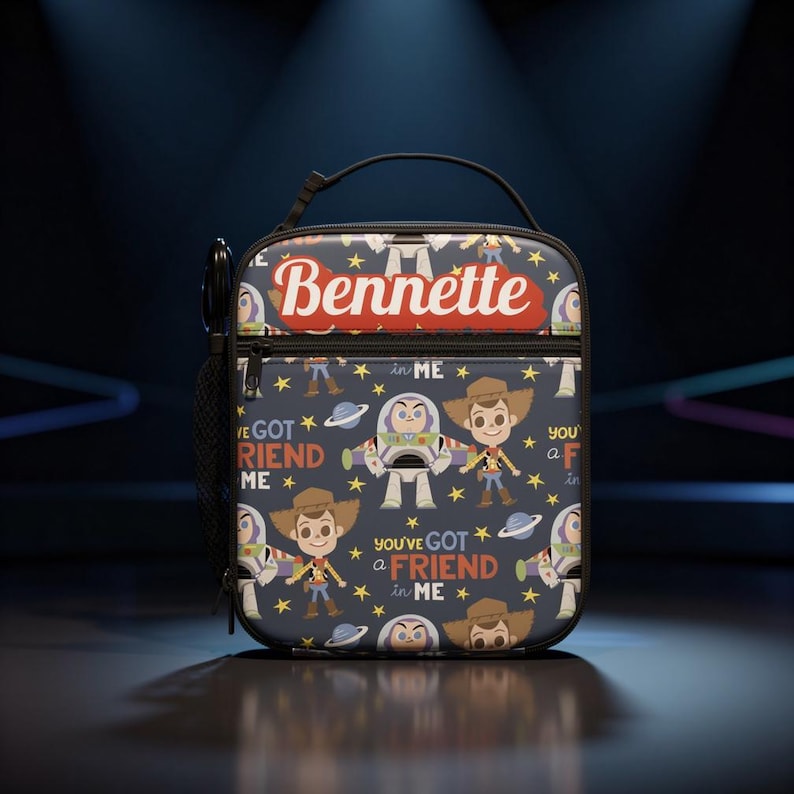 May include: A rectangular lunch bag with a dark blue background featuring a repeating pattern of cartoon characters, planets, and stars. The text "Bennette" is printed in white on a red banner, and the phrase "you've got a friend in me" is repeated.